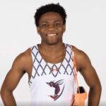 Track and field photo of Aymar Bisseck '24 with his orange cleats slung over one shoulder. Student is a BBA Sport Management concentration student at Shenandoah University. 